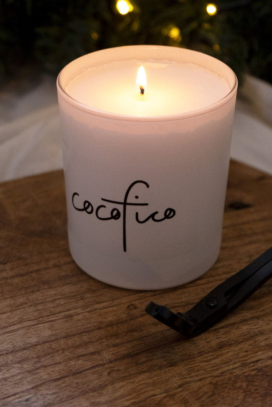Lit cocofico candle in white glass jar standing on wooden board